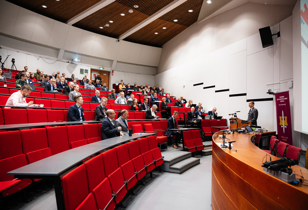 Kuvassa MPKK:n auditorio, jossa yleisöä ja kenraalimajuri Mika Kalliomaa pitämässä avauspuheenvuoroaan.