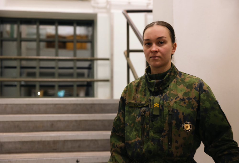 Alikersantti Maria Kaasinen katsoo vakavana kameraan. Taustalla portaikko.