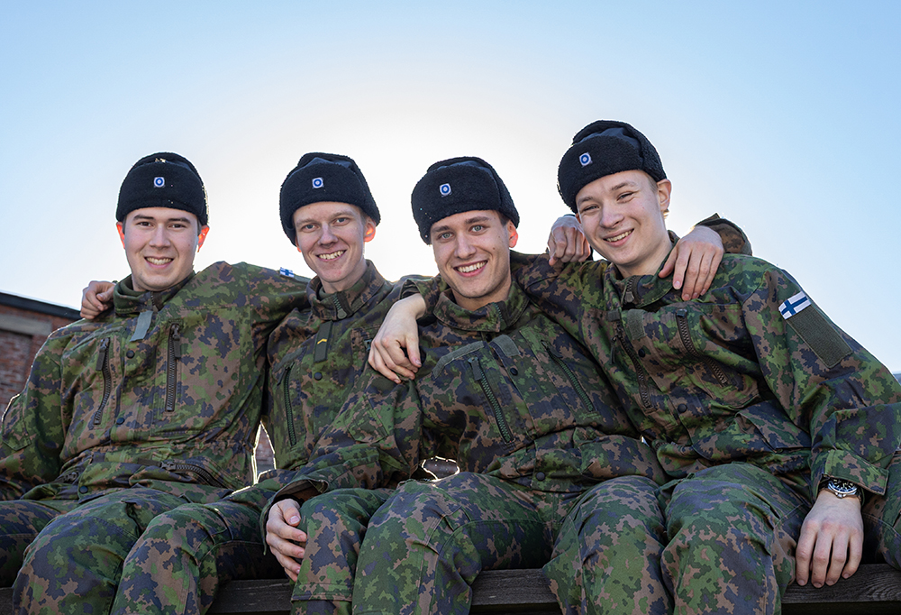 Kuvassa neljästä varusmiehestä koostuva kehittäjätiimi istuu vierekkäin toisiinsa nojaten ja hymyilee kameralle.