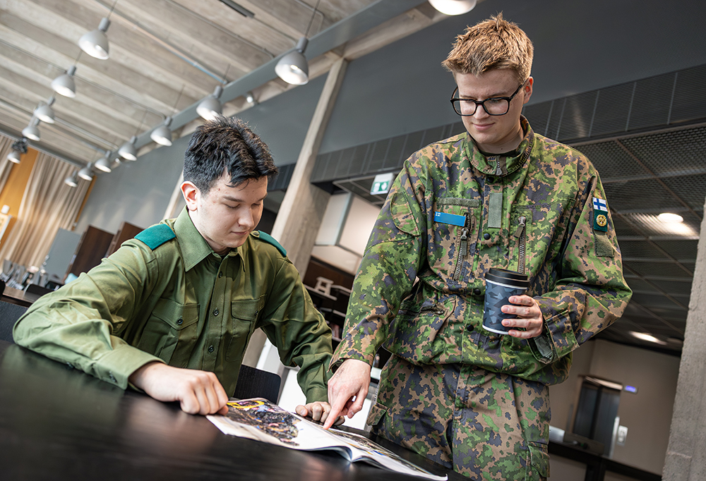 Kuvassa kaksi varusmiestä katsovat lehteä.