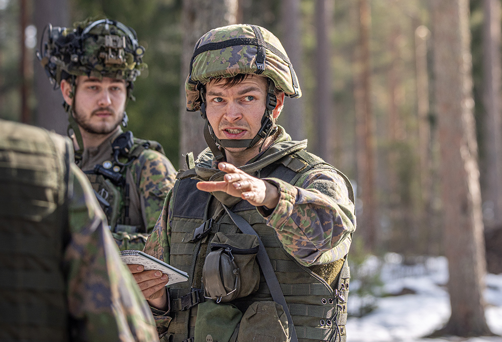 Kuvassa kaksi taisteluvarustuksessa oleva henkilö osoittaa kameraa kohti.