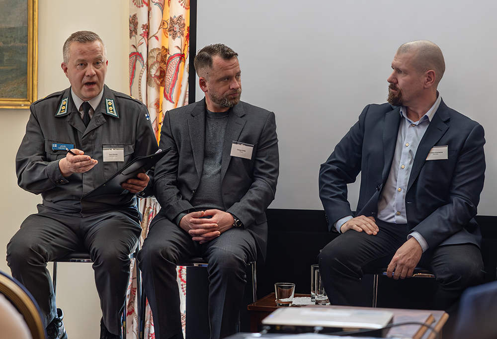 Kuvassa näkyy kolme miespanelistia istumassa penkeillä ja keskustelemassa.