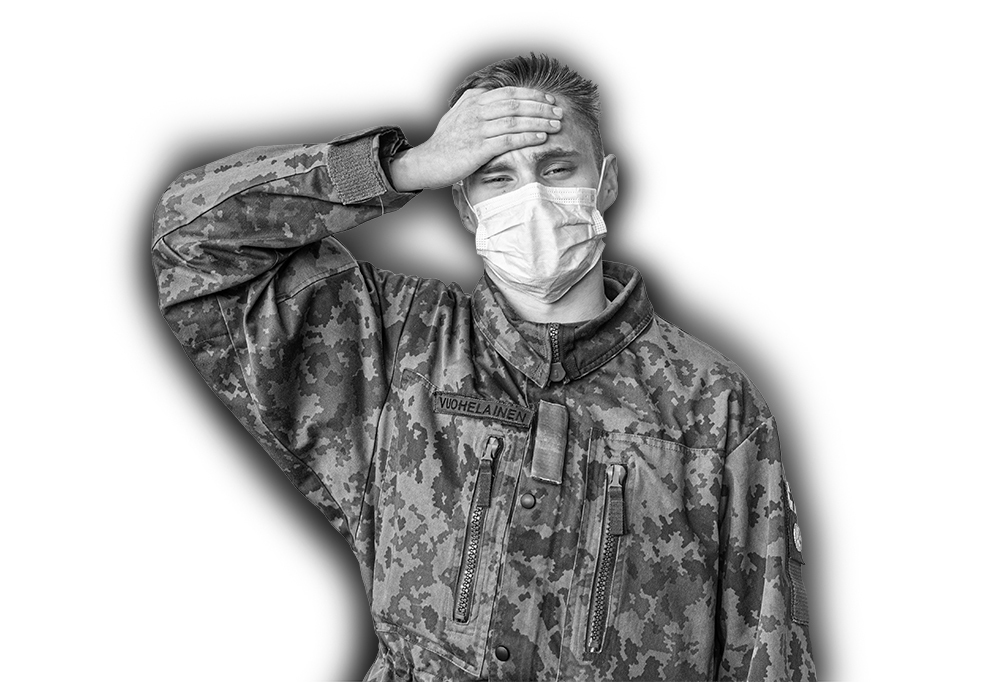 Kaartinjääkäri Vuohelainen katsoo kameraan sairaan näköisenä, kasvomaski naamalla sekä käsi otsalla.