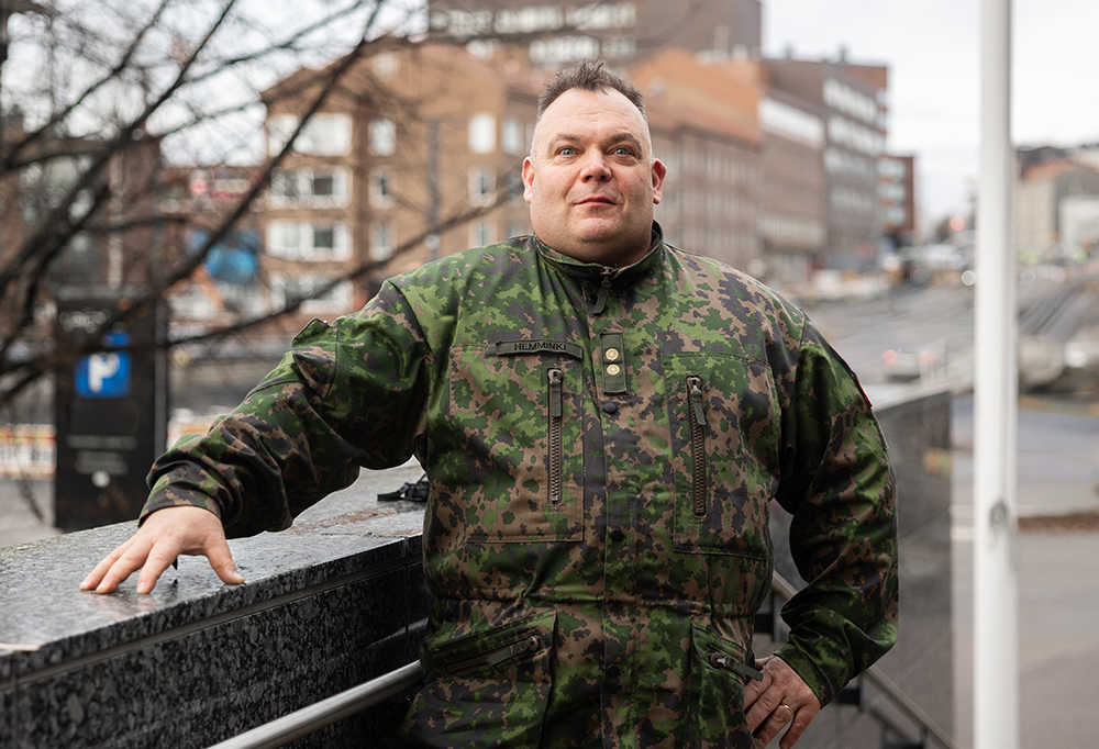 Everstiluutnantti Hemminki katsoo kameraan. Taustalla kaupunkimaisemaa.