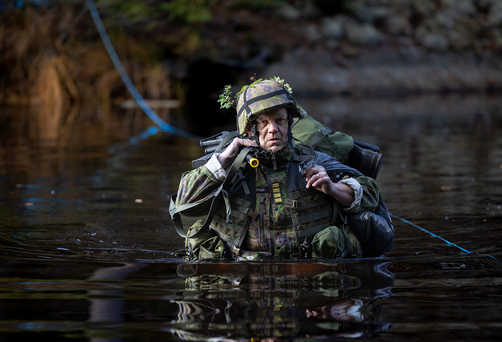 Kommodori Mikko Laakkonen ylittämässä vesistöä päällään taisteluvarustus.