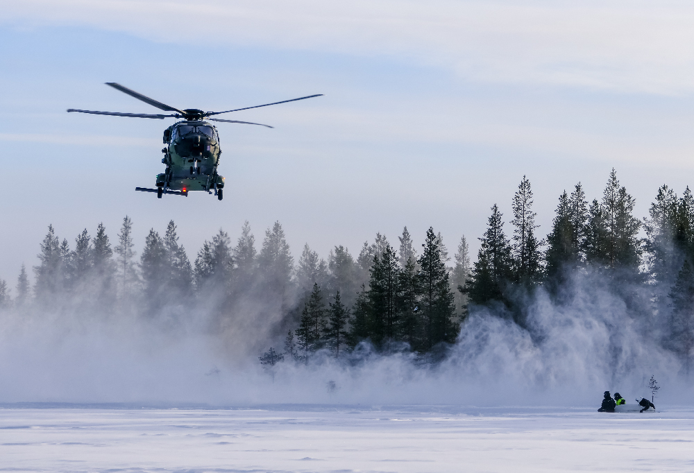 Kuvassa NH90-helikopteri lentää talvisen maaston yllä