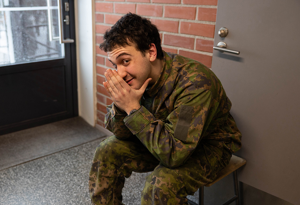 Kuvassa näkyy varusmies, joka istuu penkillä, hymyilee ja nojaa käsiinsä.