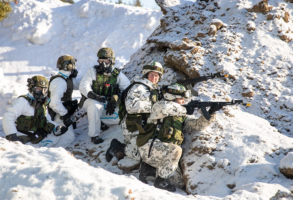 Lumipukuisia sotilailta kumpareen takana harjoituksissa.