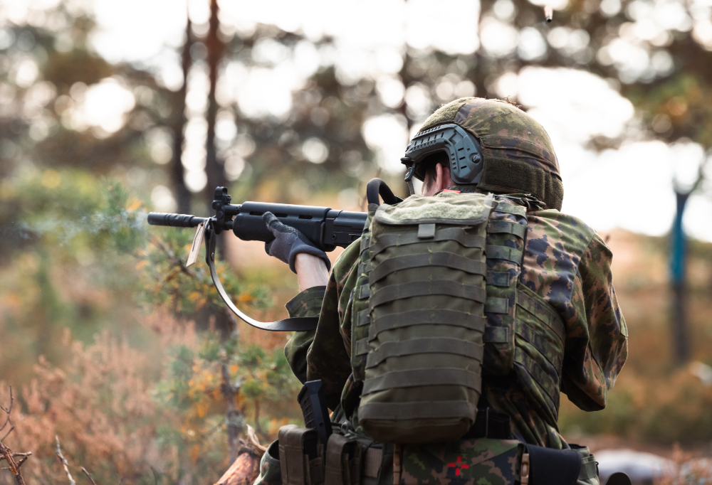 Taistelija ampumassa rynnäkkökiväärillä metsämaastossa.