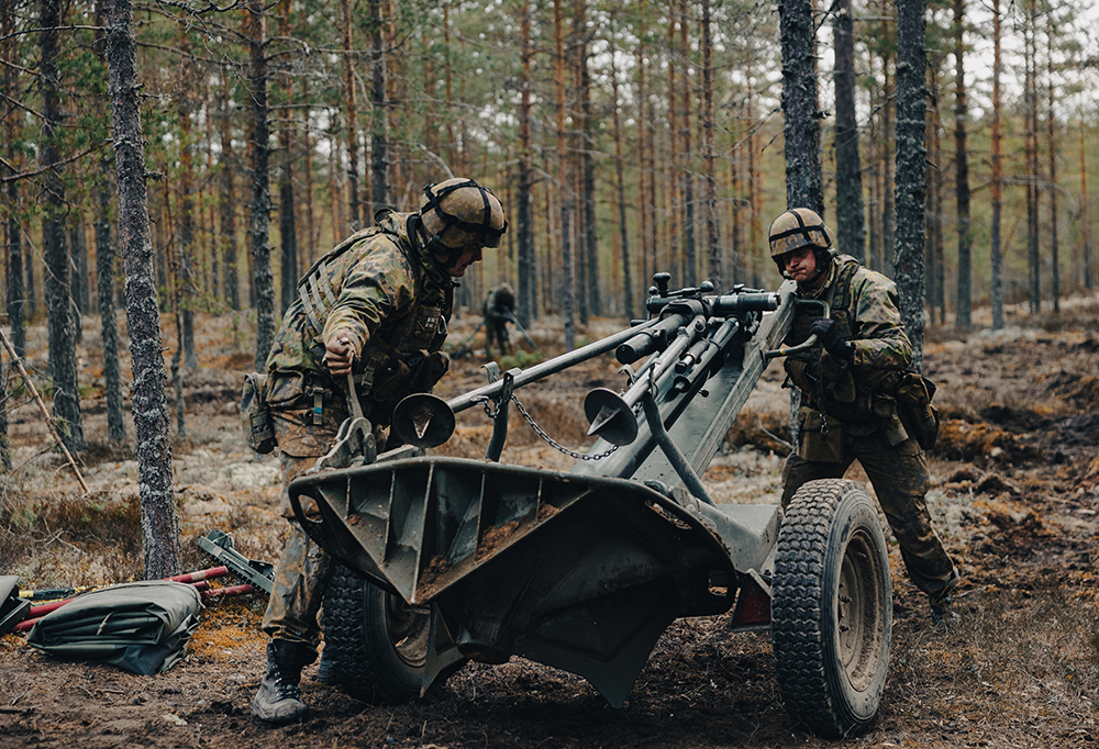 Kaksi taistelijaa käyttämässä tykkiä mäntymetsässä.