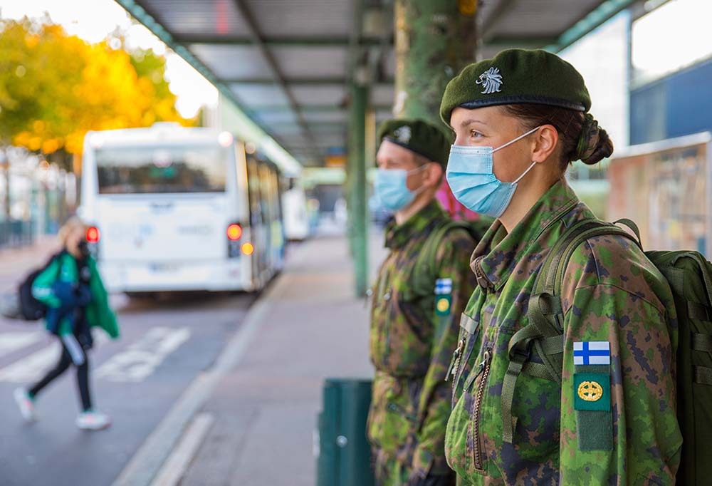 Kaksi varushenkilöä seisomassa bussipysäkillä maskit päässä.